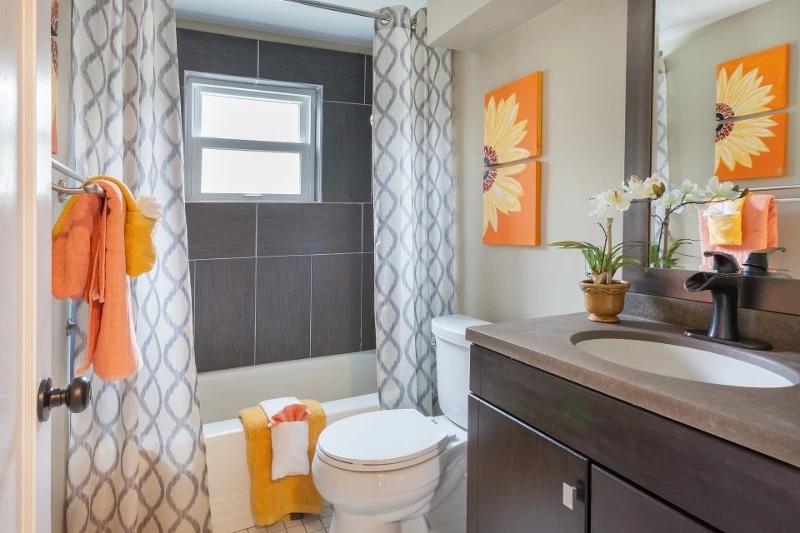 Clean Bathroom with Orange Towels and With Flower Artwork