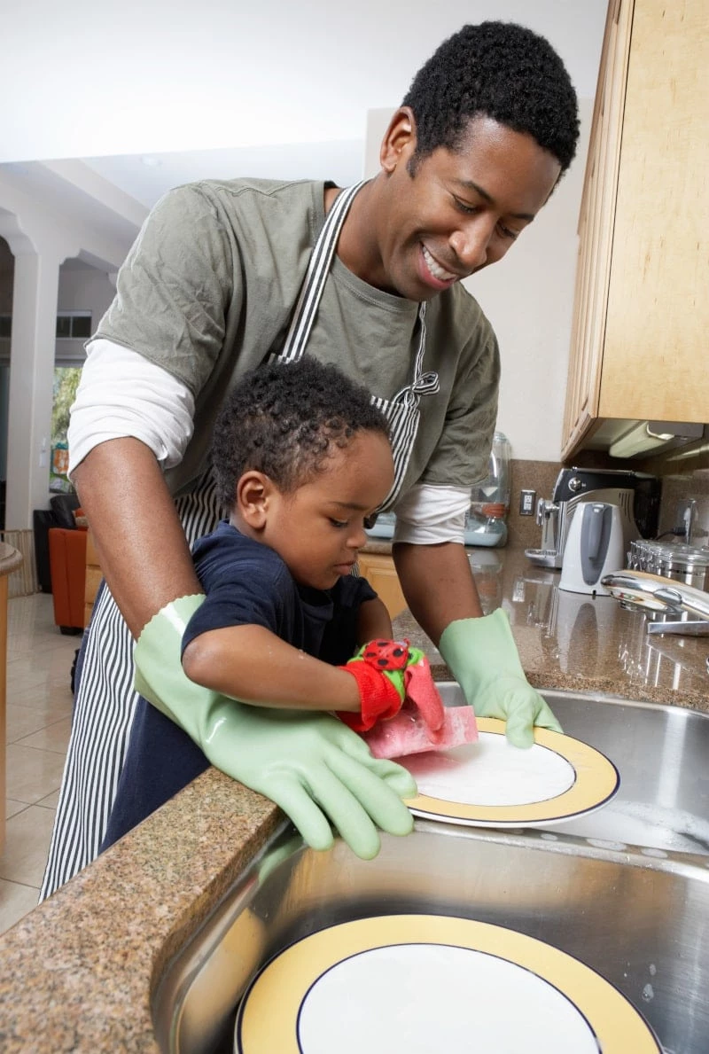 Father helping a toddler son wash dishes
