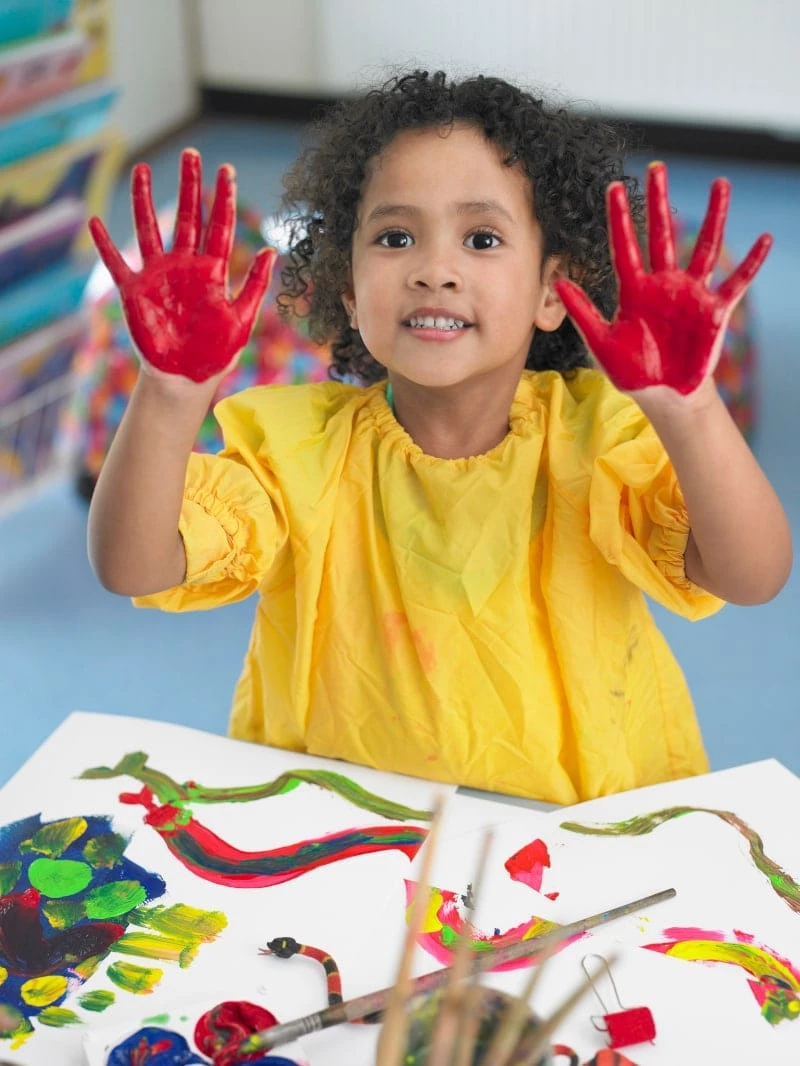 Kid with red paint on their hands finger painting with arts and crafts