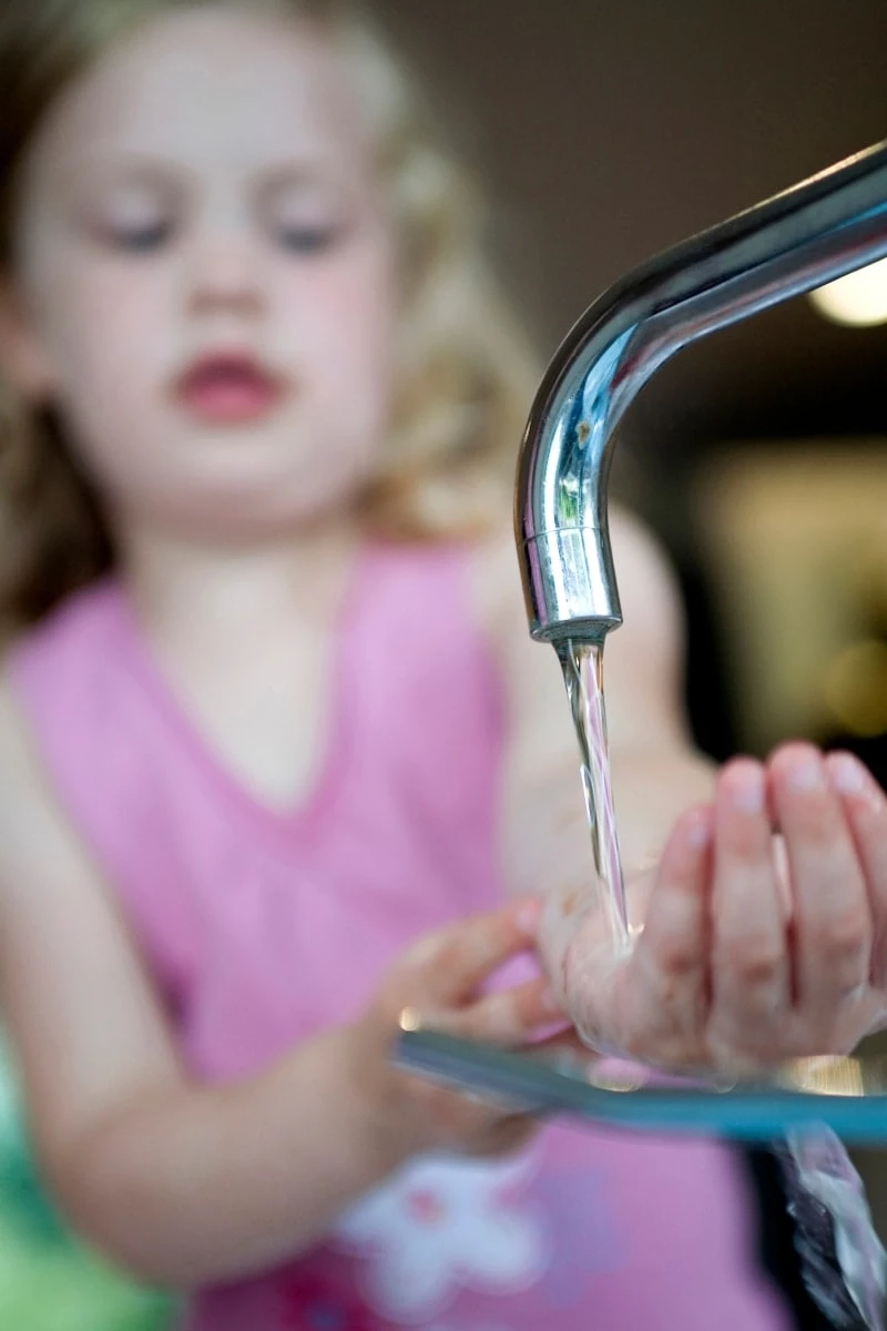 Toddler girl with hand in water at sink