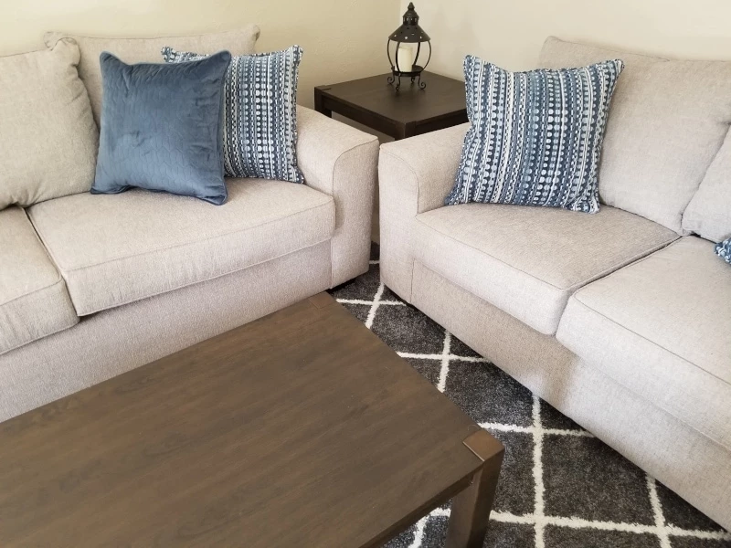 Matching grey sofa and loveseat with blue pillows grey rug and modern coffee table