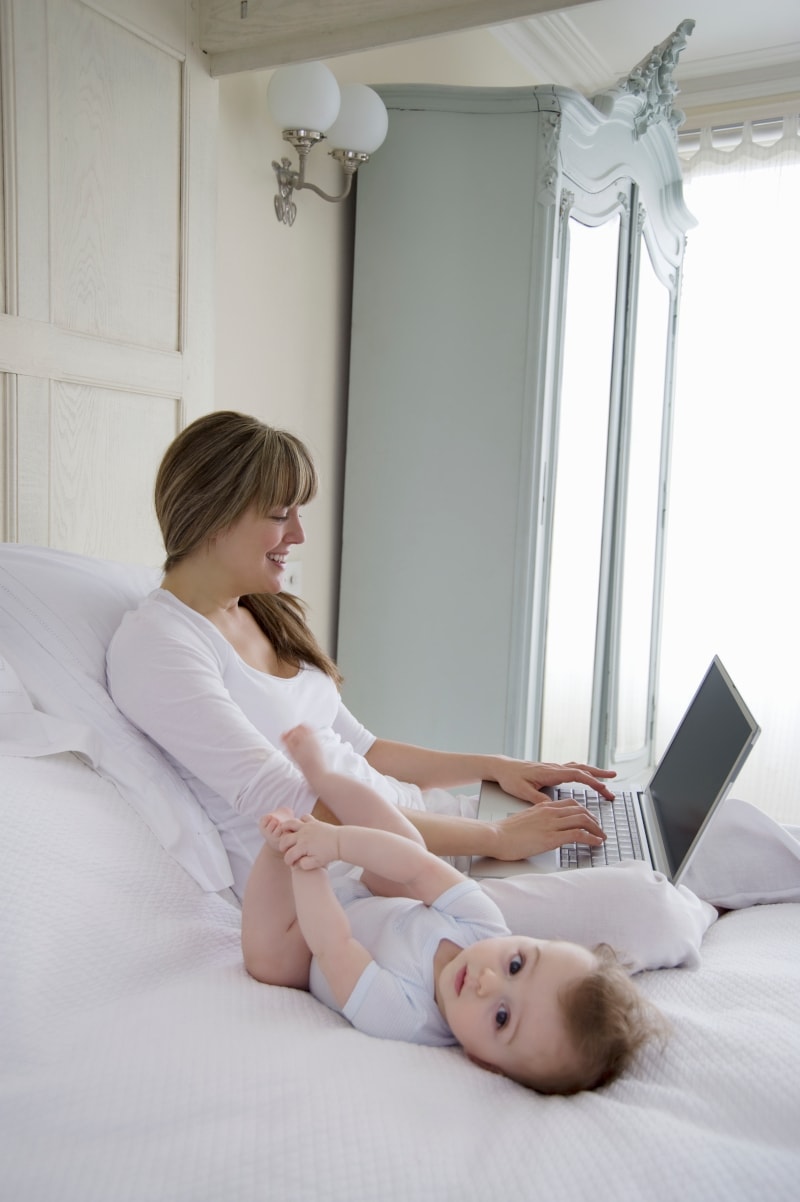 Mom working in bed on laptop with baby laying next to her