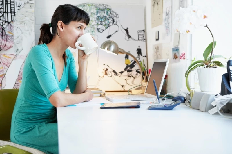 Woman in green shirt drinking coffee at desk