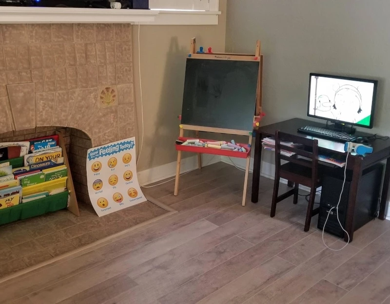 A kids desk, easel, and bookshelf in the corner of a living room for a homeschooling space