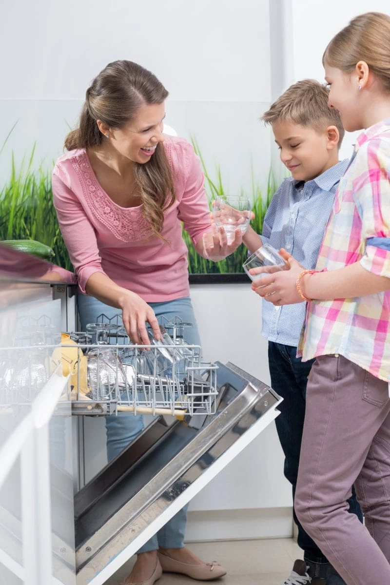 Happy mother and children placing glasses in dishwasher