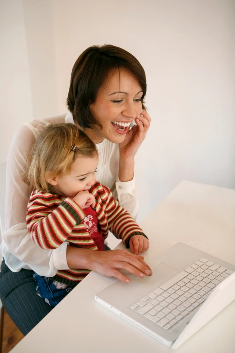 Mother on the phone while typing on the computer with her child in her lap
