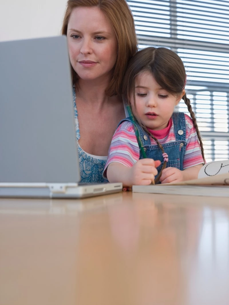 Mother working on laptop while holding a toddler in her lap