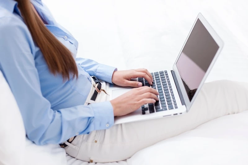 Mother Working on laptop while sitting on white sofa