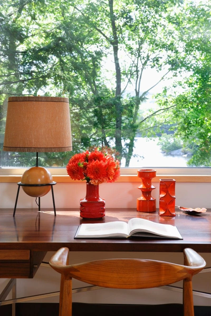 Red vases on a desk in front of a window with green leafs on trees outside