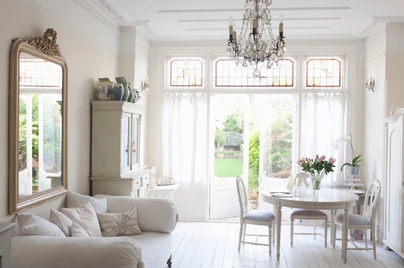 Small living room with large mirror above the sofa and a small dining table in front of a window