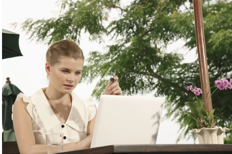 Woman in a white shirt looking at a laptop while holding a credit card