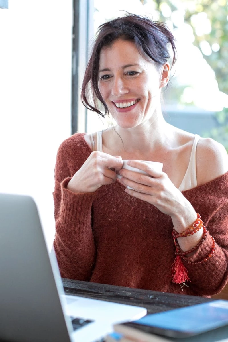 Woman in red sweater sipping coffee while looking at your laptop screen