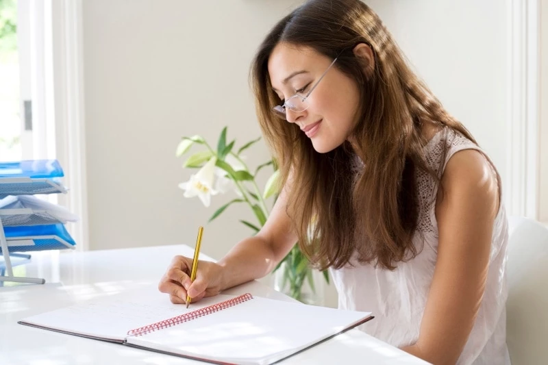 Woman wearing glasses writing in a planner