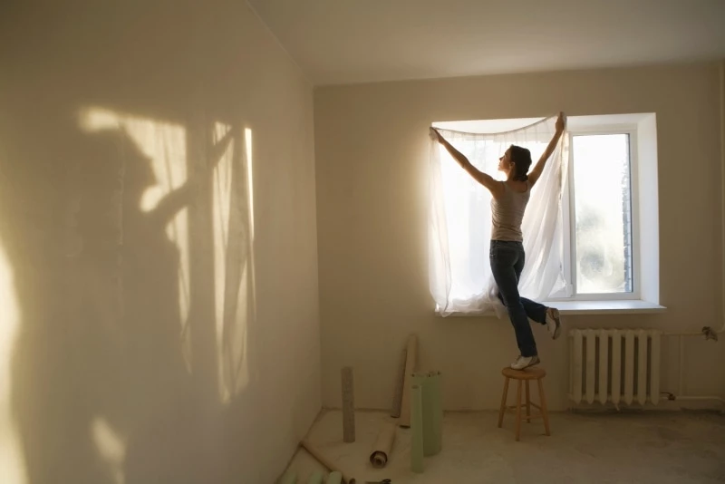 woman hanging sheer white curtains in a window