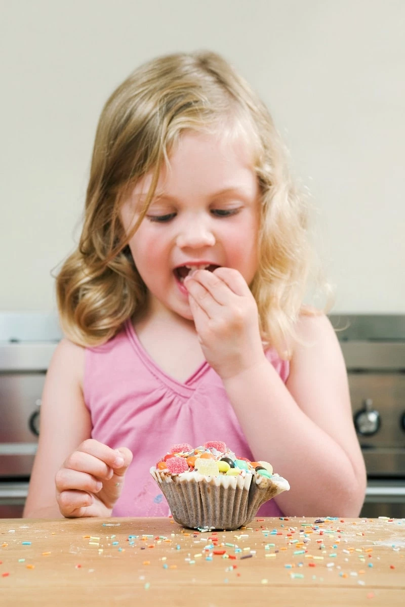 4 year old girl eating sprinkles off a cupcake