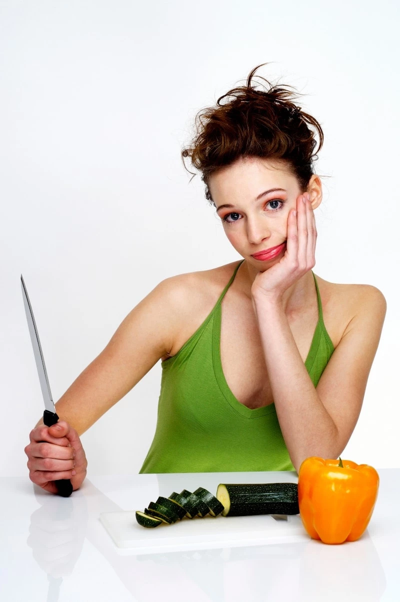 woman holding a knife and slicing cucumber and bell pepper