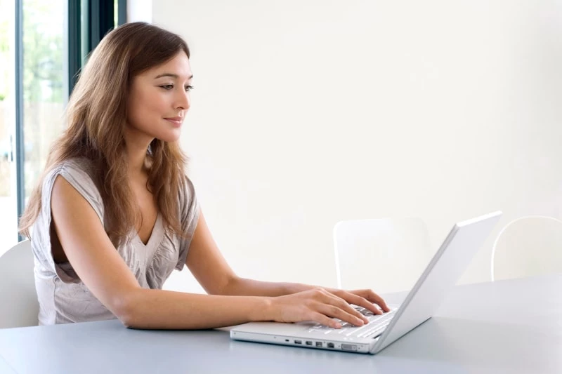 Woman sitting at a table typing on a laptop
