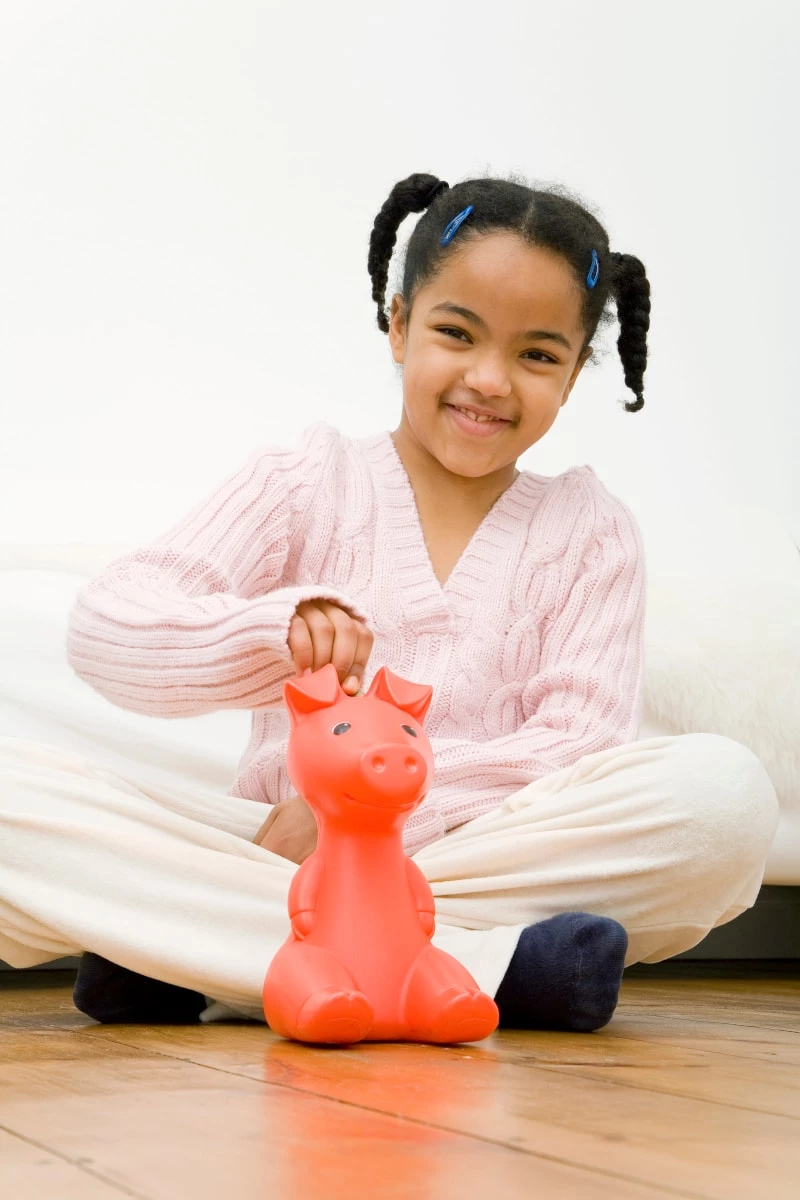 Young female child putting money into a hot pink piggy bank