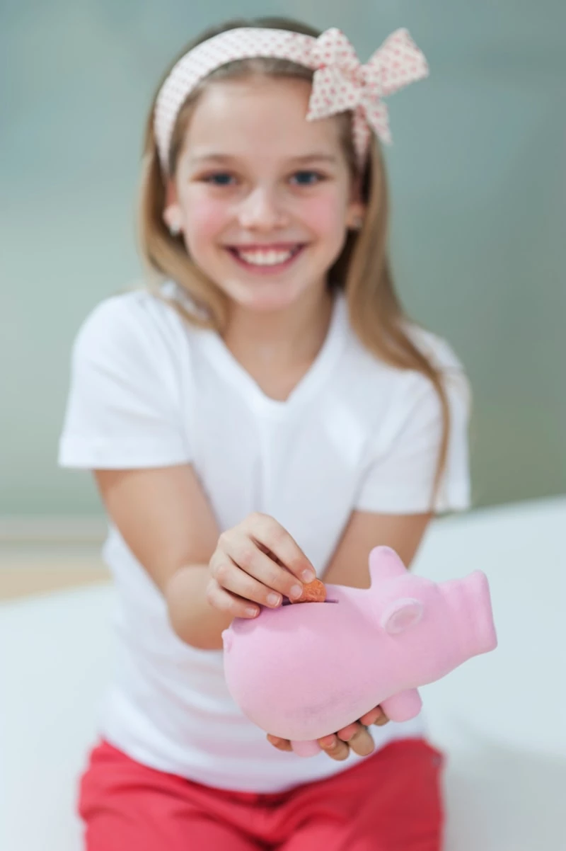 Portrait of a happy girl putting coin in piggy bank