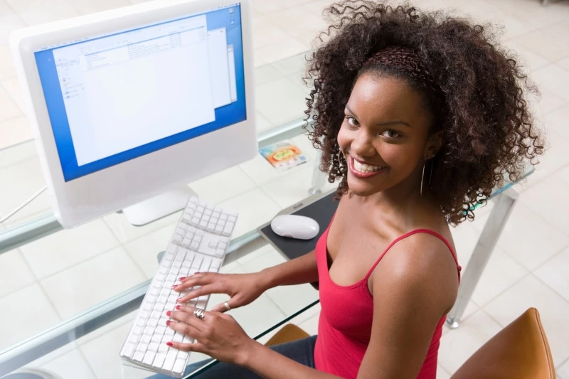 woman smiling at a camera while typing on a computer