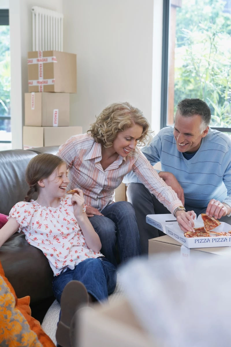 A mom, dad, and daughter, sharing a pizza in their living room