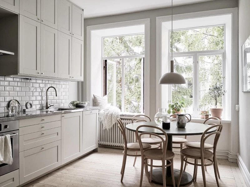 A Scandinavian styled eat in kitchen with white cabinets and white subway tile and a minimalist design.
