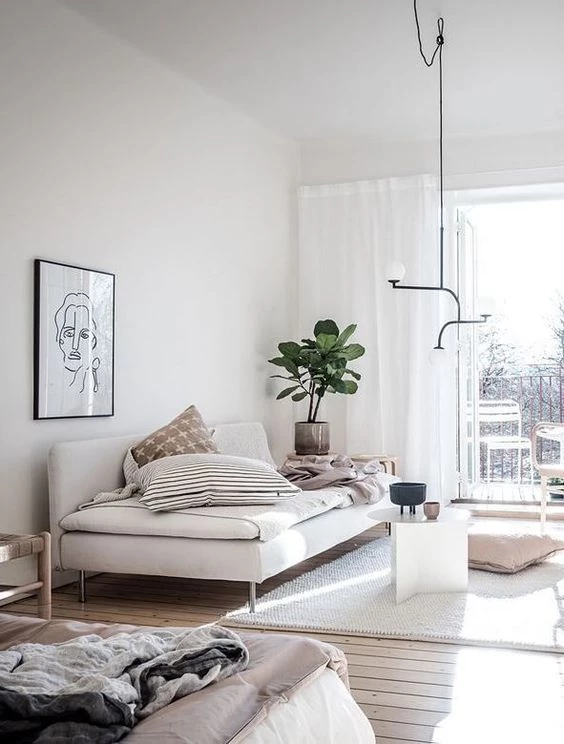 A Scandinavian styled living room with minimalist artwork and lighting, a simple modern white sofa, a small geometric coffee table, and a plant in the corner.