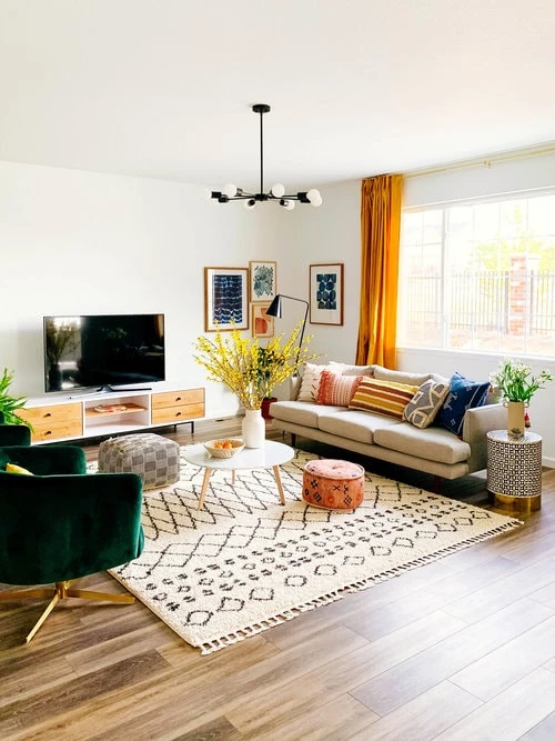 Mid century style furniture mixed with bohemian patterns in poofs, pillows, and rugs. The grey couch is paired with a white round coffee table and two emerald green chairs with gold stands.