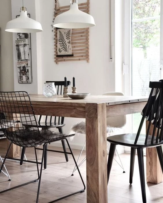 A Scandinavian styled dining room with mis-matched black and white chairs and a natural wood toned table.