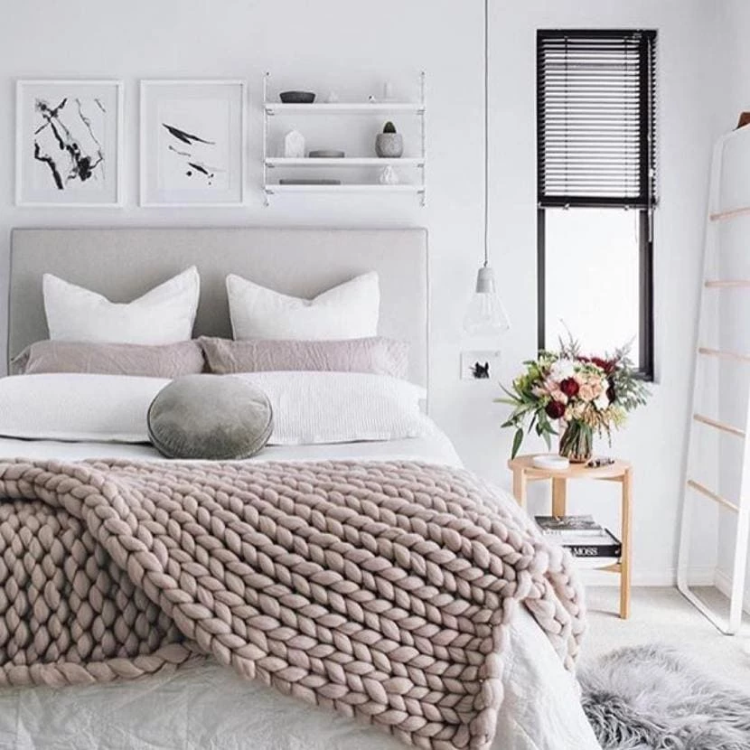 A Scandinavian styled bedroom with soft white plush bedding and a faux fur rug.