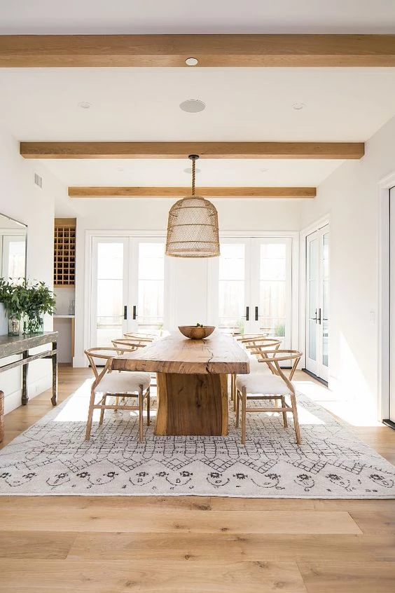 A Scandinavian styled dining room with a large rug and a raw edge large dining table with 3 chairs on either side.