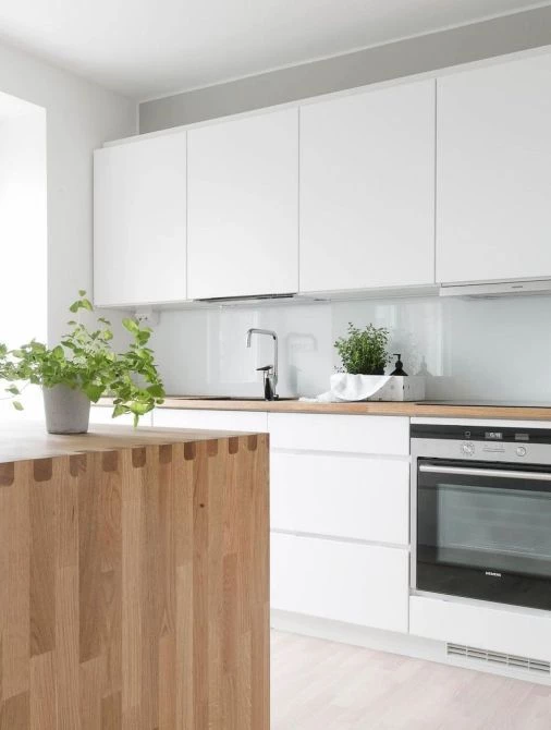 A Scandinavian styled kitchen with white cabinets and natural wood tones in the countertop and island. Two small plants sit on the counters.