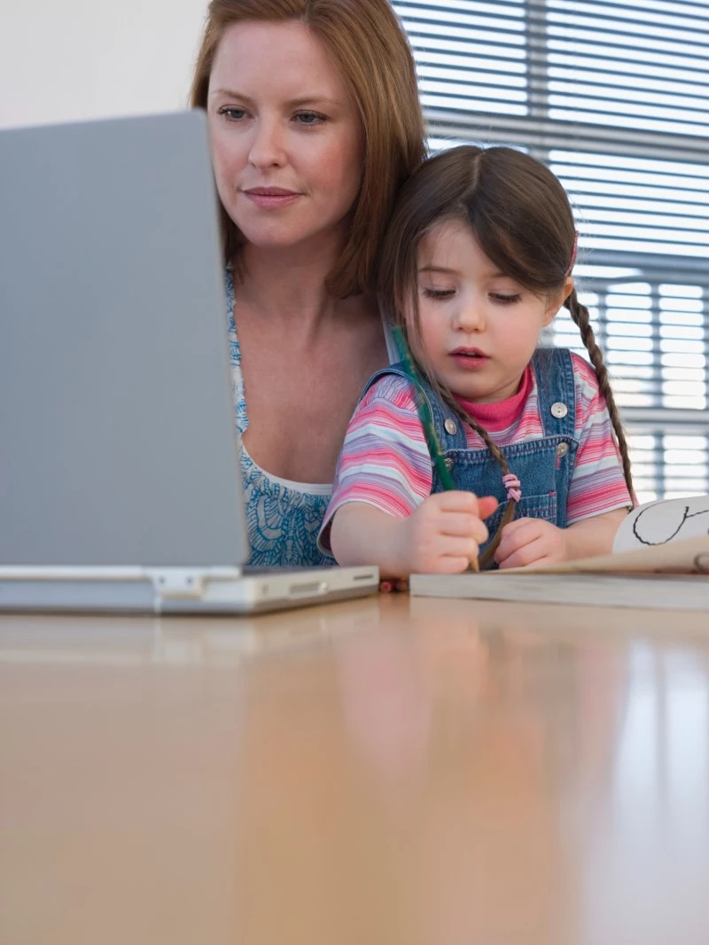 woman holding child in lap while typing on a laptop