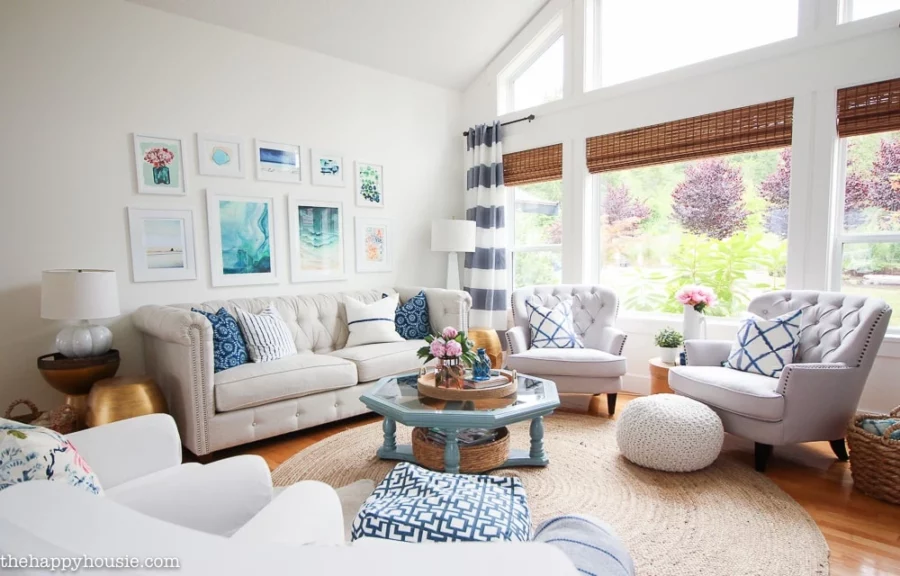 Living room with woven rug, off white and white chairs, blue accents, and beach artwork gallery wall