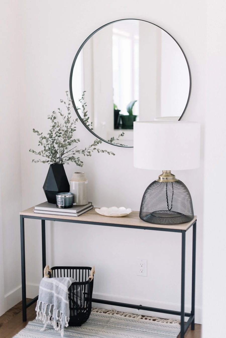 A modern front entryway using black accents on a slim table. Black framed circular mirror hangs above the table.