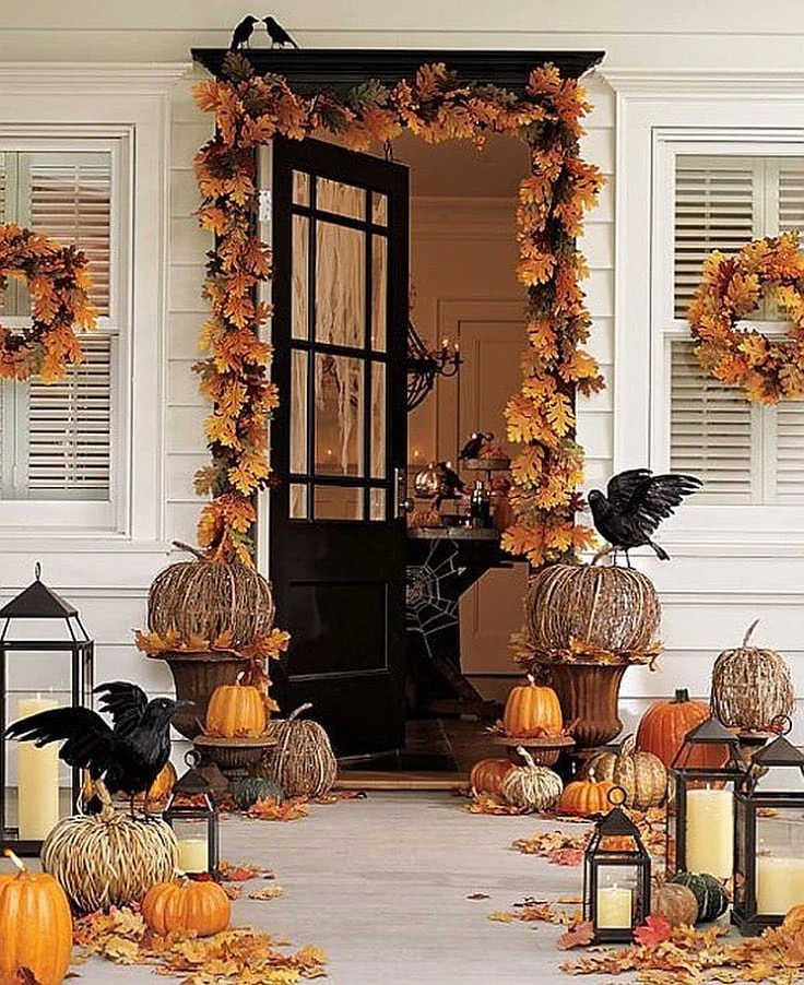 A front porch with straw pumpkins, real pumpkins, fake crows, orange leaves, and lanterns with candles