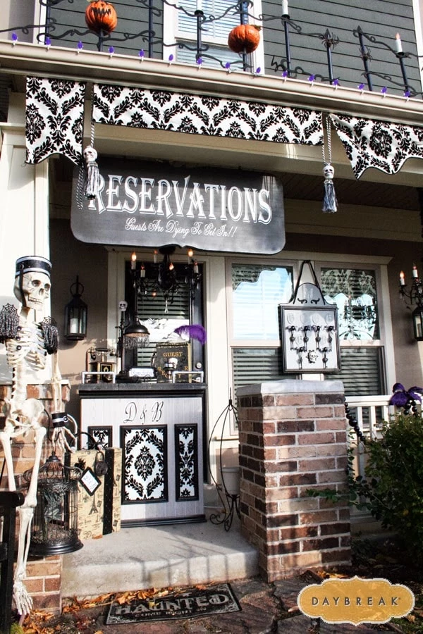 A front porch with a reservations sign, a skeleton door man, purple feathers, and chandeliers for a creepy looking bed and breakfast look