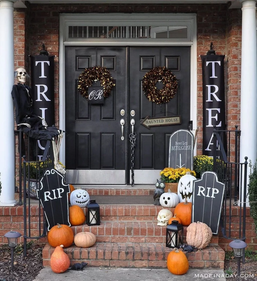 Front porch with gravestones, pumpkins both orange and white, and a skeleton.