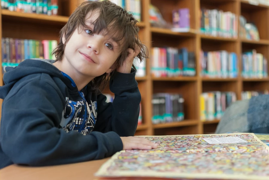 child smiling at the camera sitting in a library with books on the table