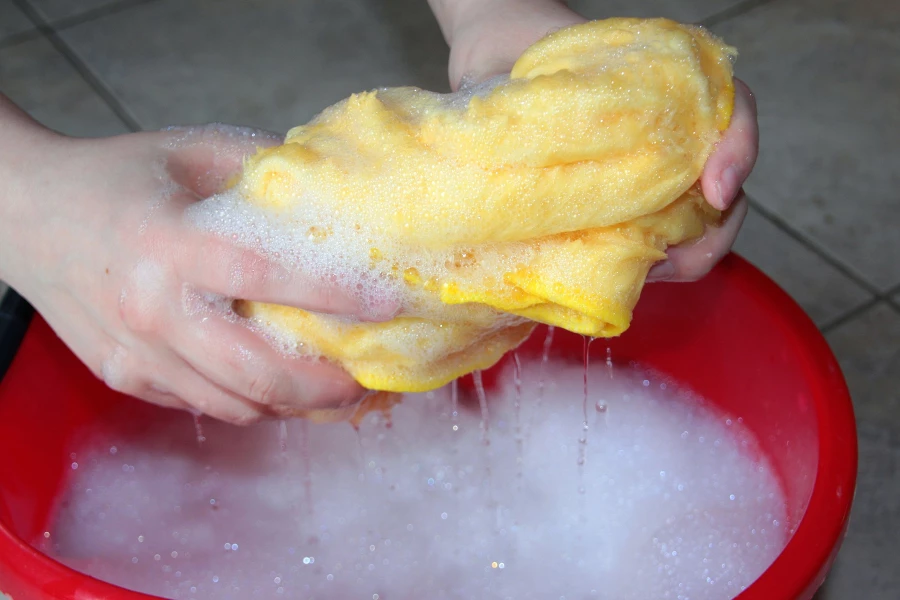 a yellow rag being rung out over a red bucket filled with soapy water