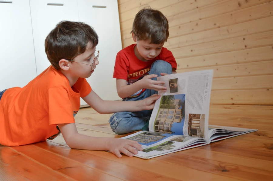 two kids reading a book on a wood floor